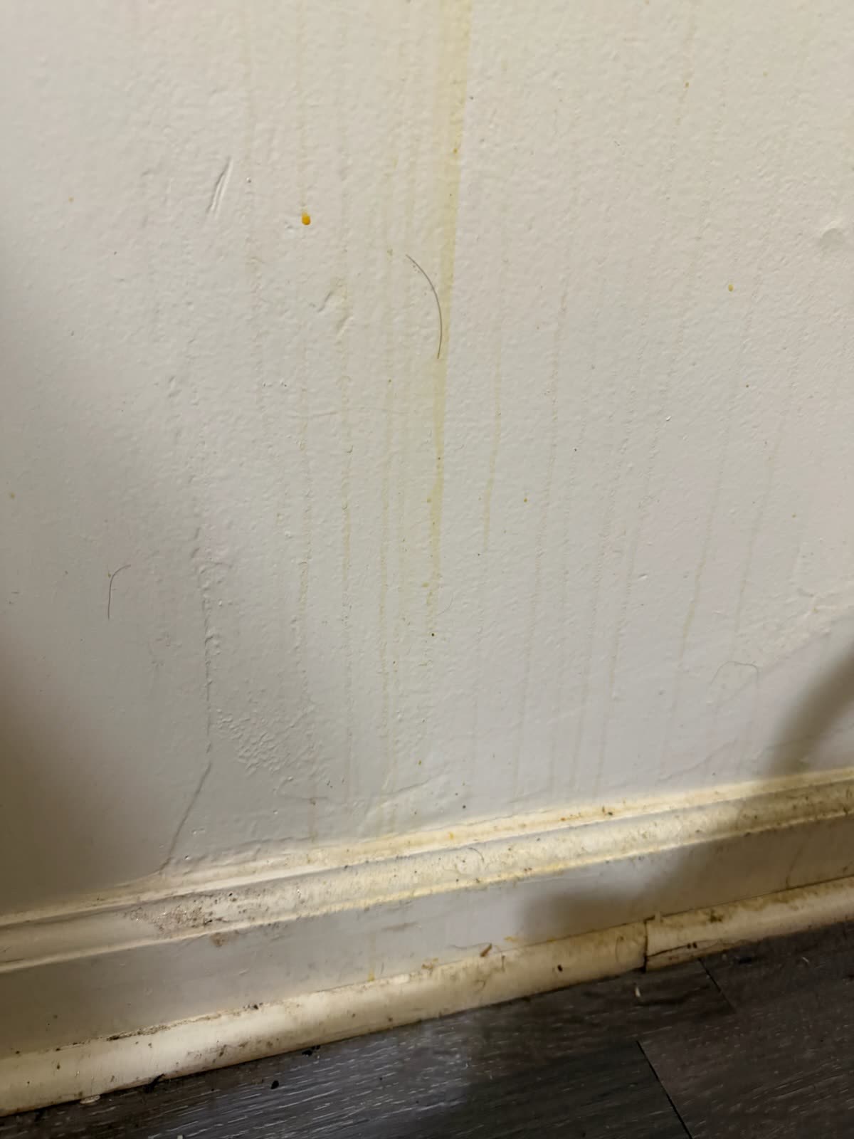 Wall and baseboard with drip stains and grime before cleaning